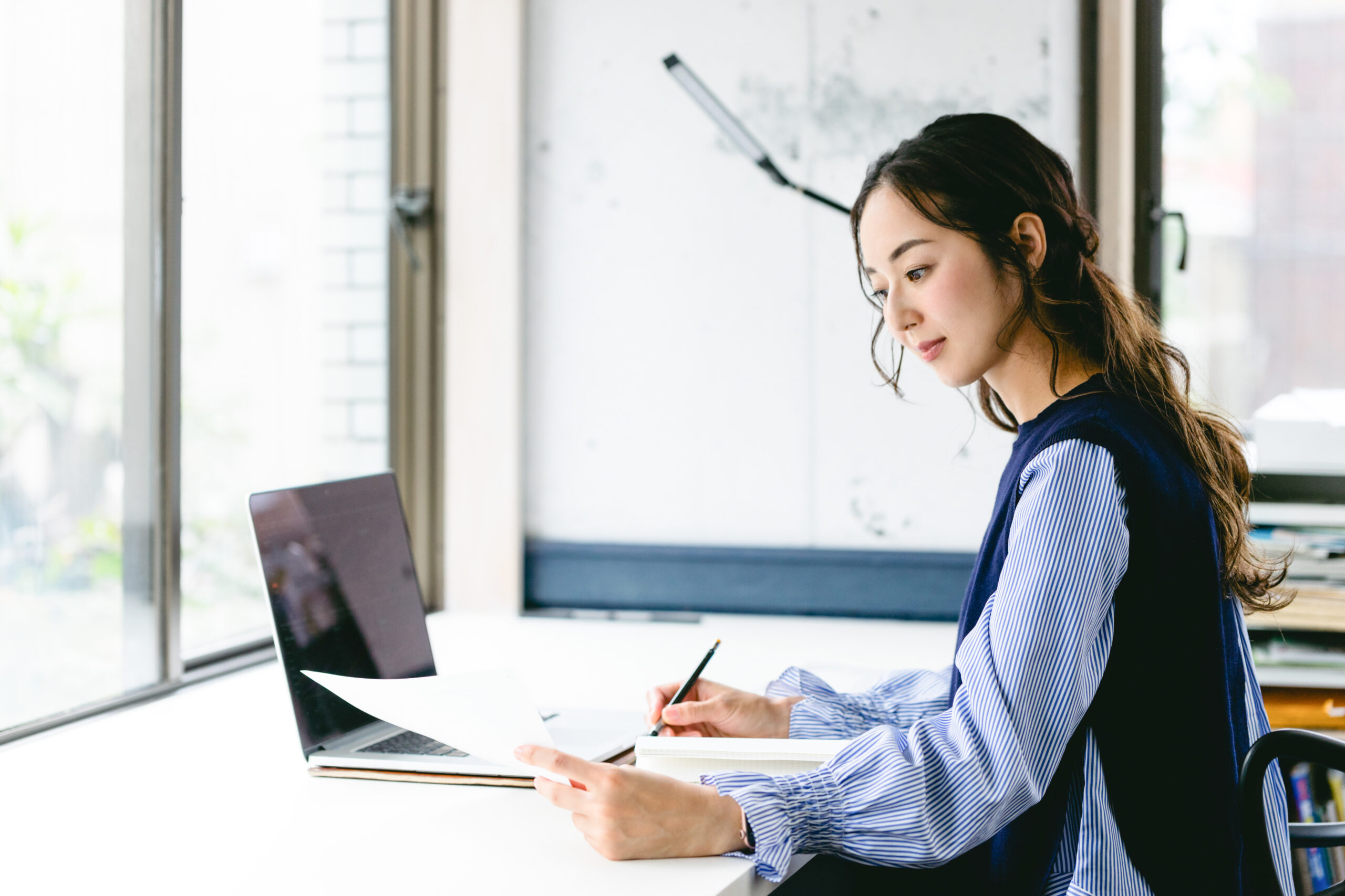 パソコンと資料を前に考える女性