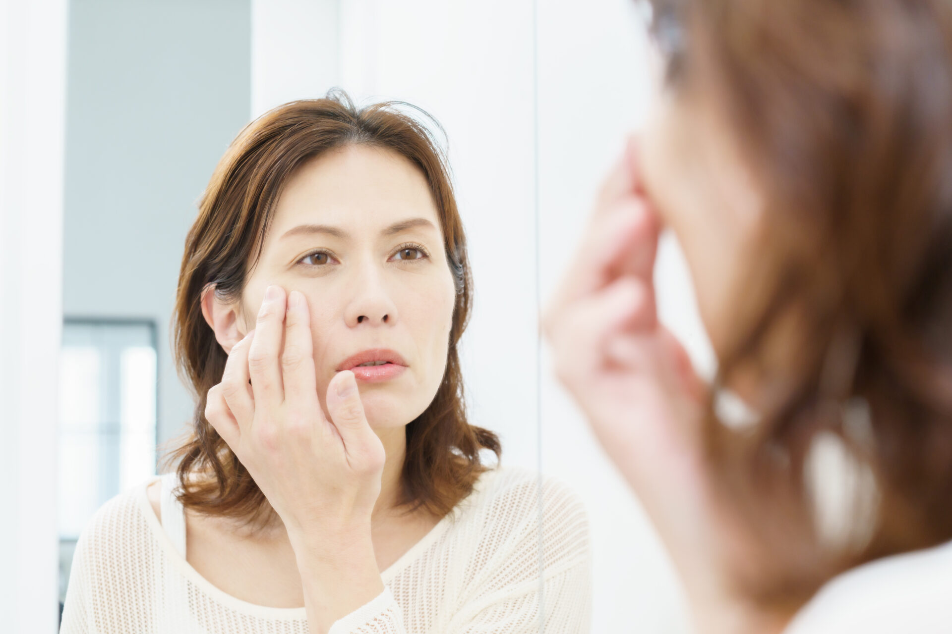 鏡を見ながら自分の顔の変化を気にする女性